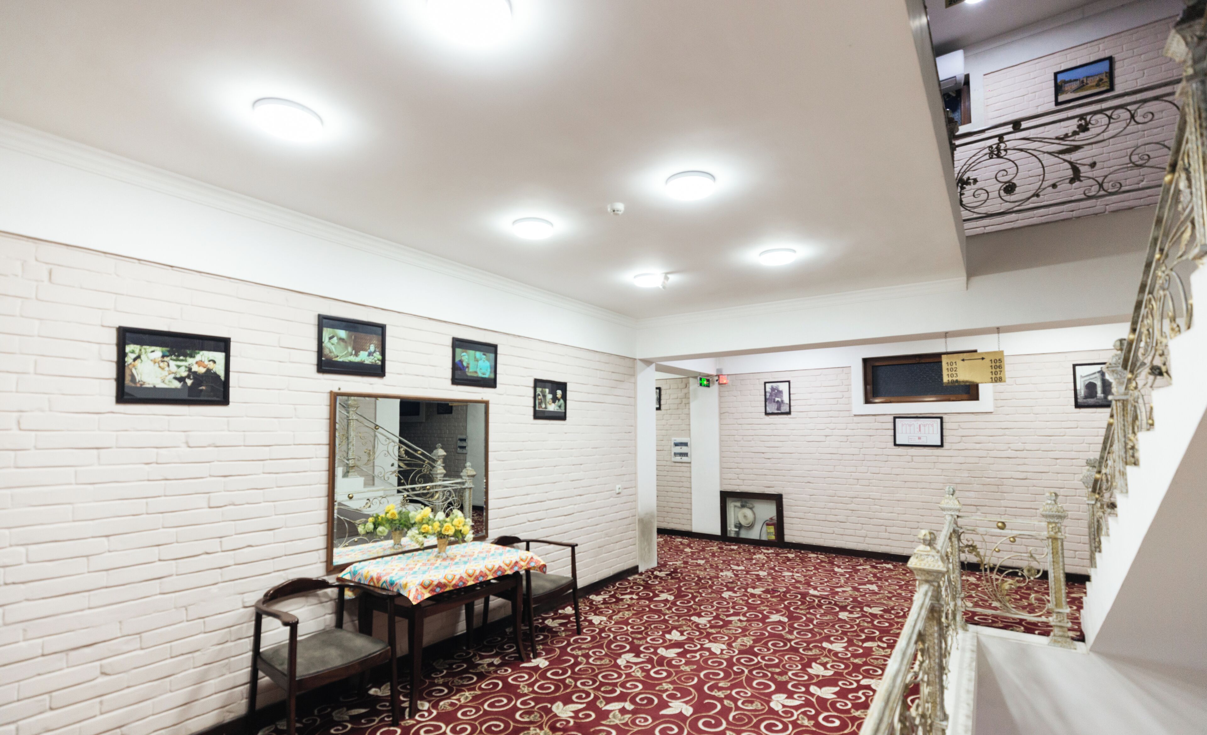 A room with white brick walls, a patterned carpet, a dining table with chairs, and framed pictures on the walls.