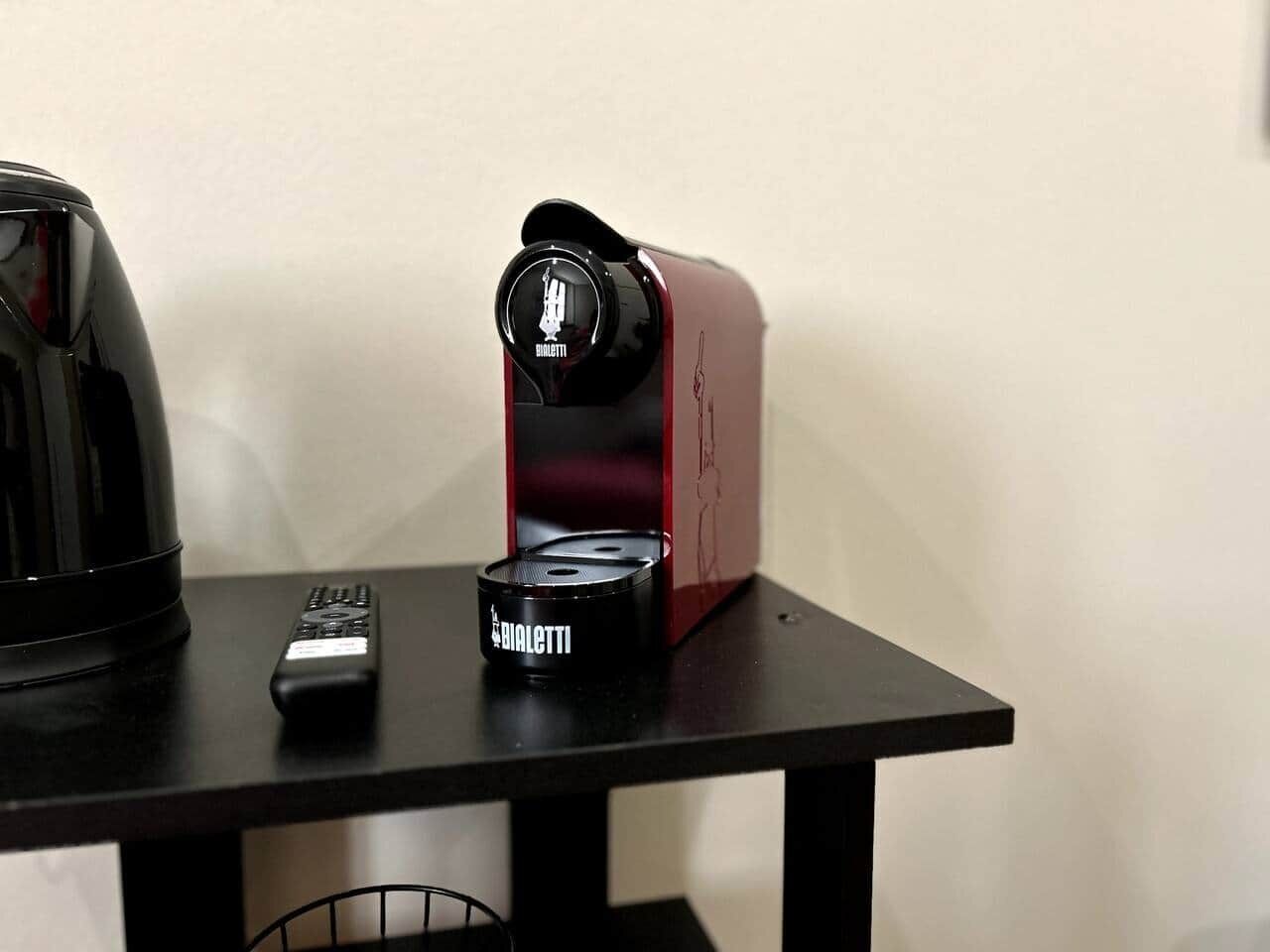 A black coffee maker, a red appliance, and a remote control on a black table.