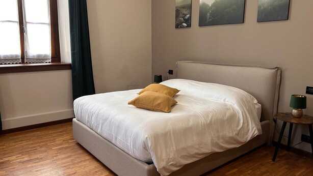 A bedroom with a bed, wooden flooring, a window with curtains, and wall-mounted artwork. - Stanza d'epoca (Volta Mantovana) Stanza in dimora two steps from Lake Garda (Volta Mantovana)
