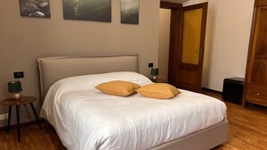 A neatly made bed with two pillows, a wooden floor, a nightstand with a lamp, and a door with a golden handle. - Stanza d'epoca (Volta Mantovana) Stanza in dimora two steps from Lake Garda (Volta Mantovana)