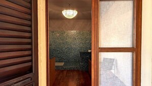 Een houten deur die leidt naar een badkamer met een betegelde muur, een douche en een hangende lamp.