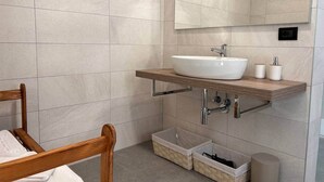 Un baño con una silla de madera, un lavamanos blanco, un espejo y dos cestos de almacenamiento.