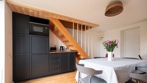 Eine moderne Küche mit dunklen Schränken, einer Holztreppe, einem Esstisch mit Stühlen und einer Vase mit Blumen.