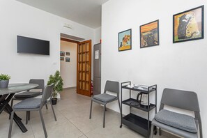 Ein Zimmer mit Esstisch, Stühlen, einer Kaffeemaschine, einem Fernseher und Bildern an den Wänden.