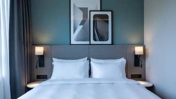 Een hotelkamer met een bed, twee wandlampen en twee abstracte kunstwerken in lijsten aan de muur.