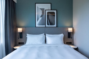 Une chambre d’hôtel avec un lit, deux lampes fixées au mur et deux œuvres d’art abstraites encadrées accrochées au mur.