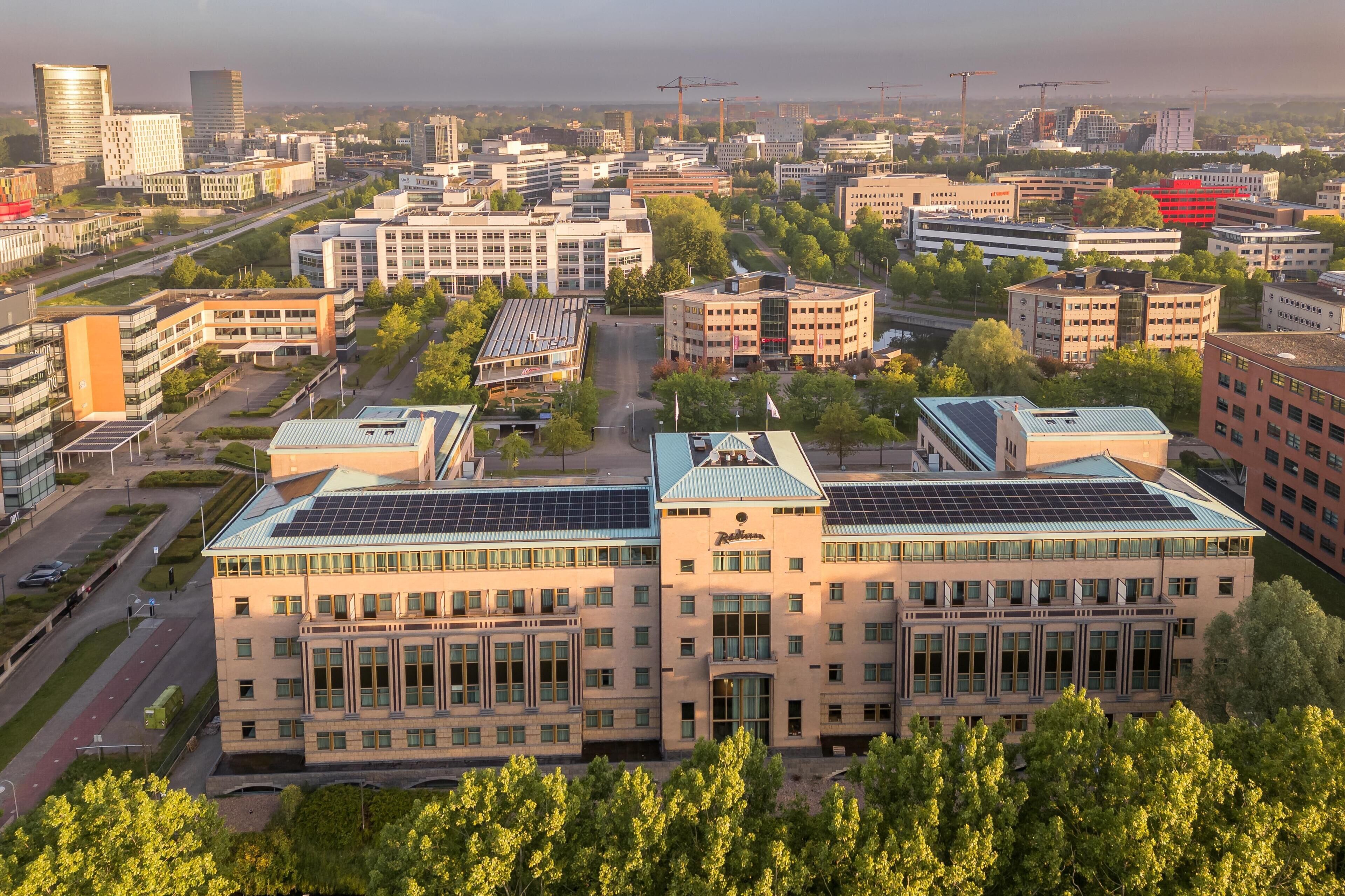 Ein mehrstöckiges Gebäude mit einem zentralen Innenhof, umgeben von weiteren Gebäuden, und Solaranlagen auf dem Dach.