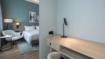 A hotel room with a bed, bedside table, lamp, chair, desk, and a wall-mounted picture.