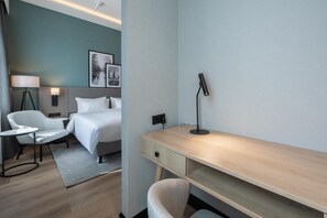 Une chambre d’hôtel comprenant un lit, une table de chevet, une lampe, une chaise, un bureau et un tableau accroché au mur.