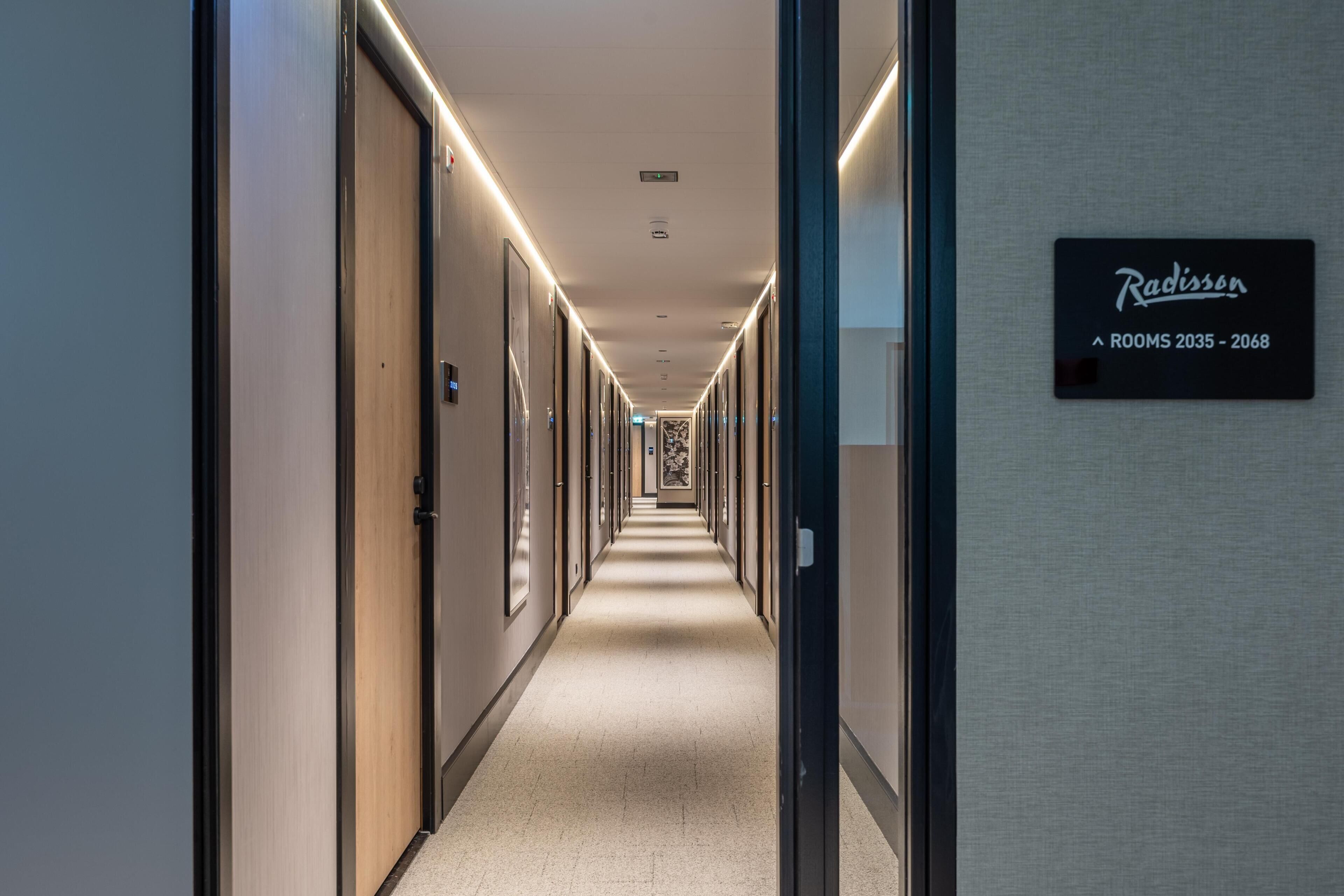 Een hotelgang met deuren aan beide kanten, een bord met de cijfers 2035-2068, en een patroon op het einde van de muur.