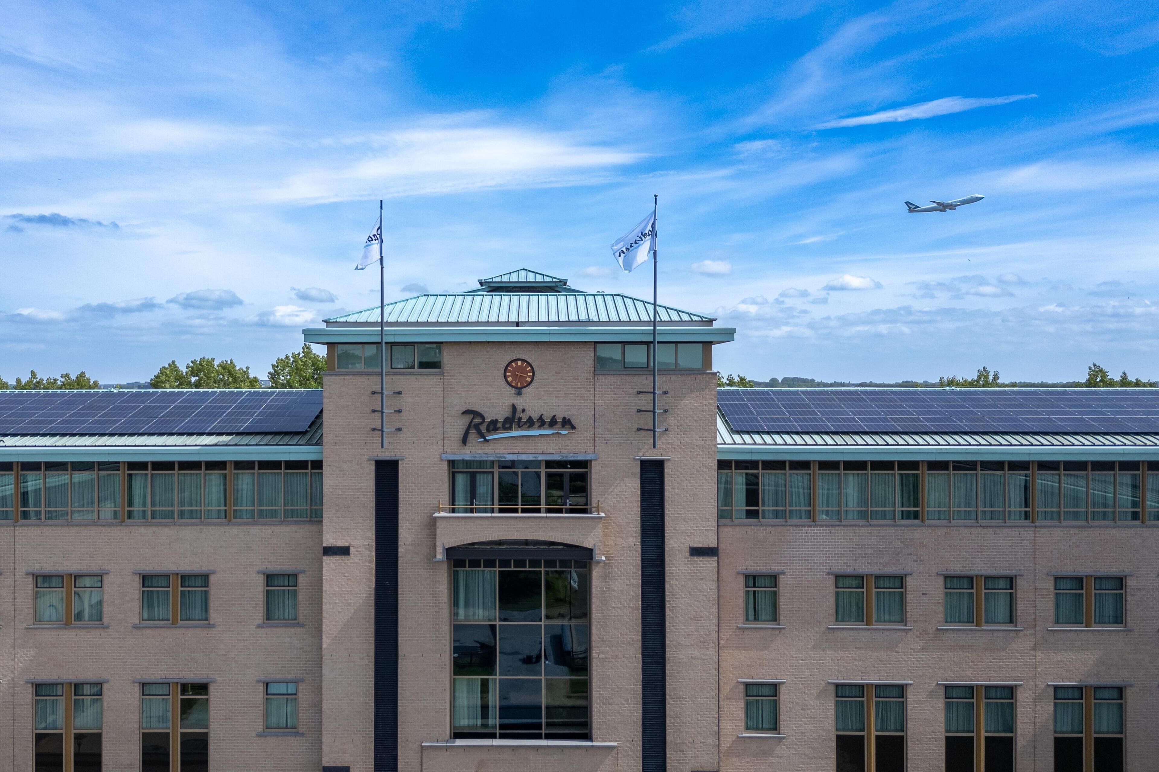 Un edificio con entrada central, dos banderas y techo con paneles solares.