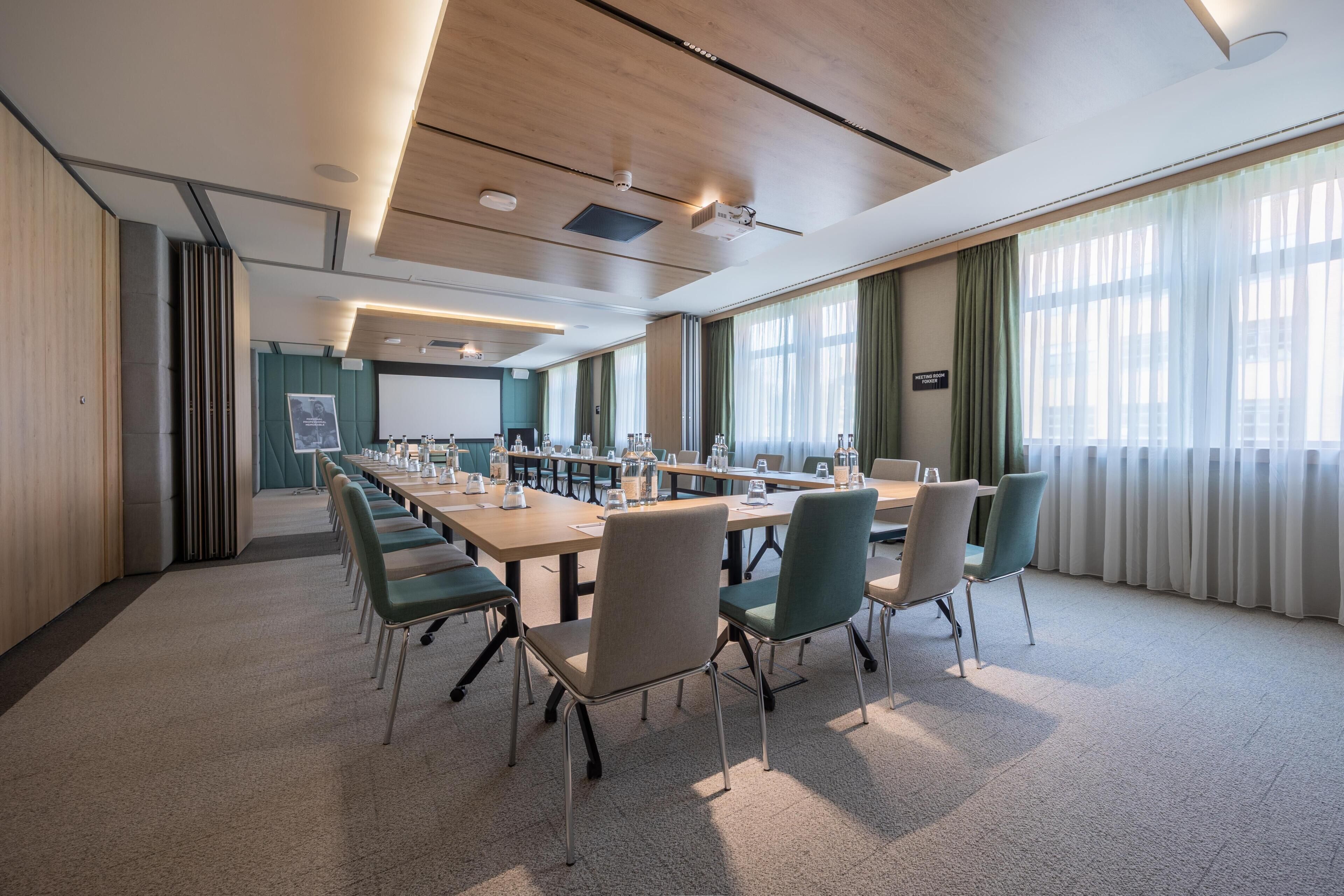 A conference room with a long table, chairs, and a projector screen.