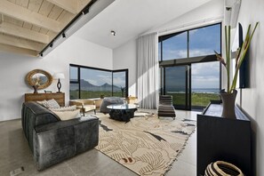 A modern living room with a large window, a sofa, a coffee table, and a rug. - Ocean 9 Beachfront Residence (Cape Town)