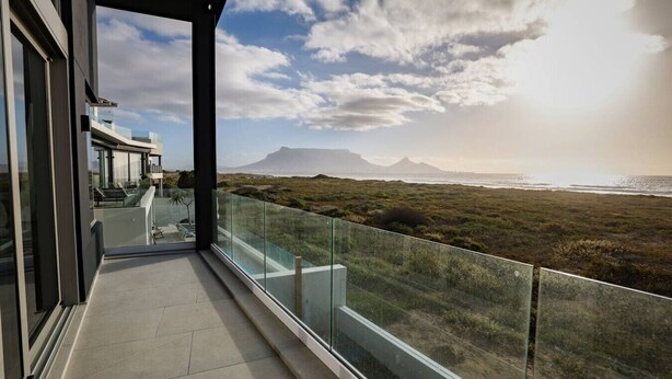 Ein moderner Balkon mit Glasgeländern, der auf eine Küstenlandschaft mit Bergen im Hintergrund blickt.