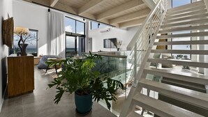 Ein modernes Interieur mit einer Wendeltreppe, einer großen Topfpflanze und Meerblick.
