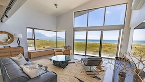 A modern living room with a large window overlooking a coastal landscape, a glass coffee table, and a leather sofa.
