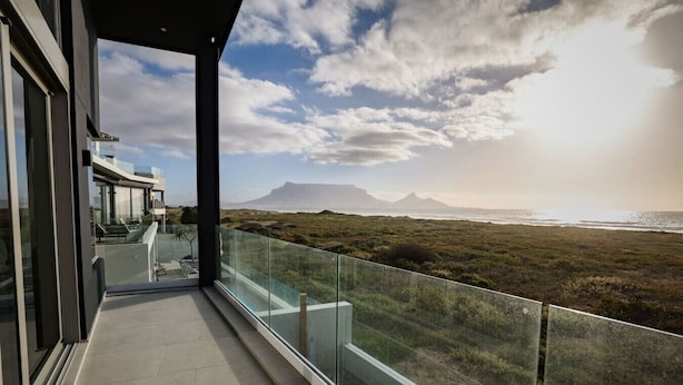 A modern balcony with a glass railing overlooking a coastal landscape with mountains in the distance.