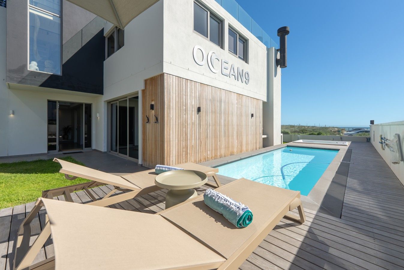 Un bâtiment moderne doté d’une piscine, d’une terrasse en bois et de chaises longues.