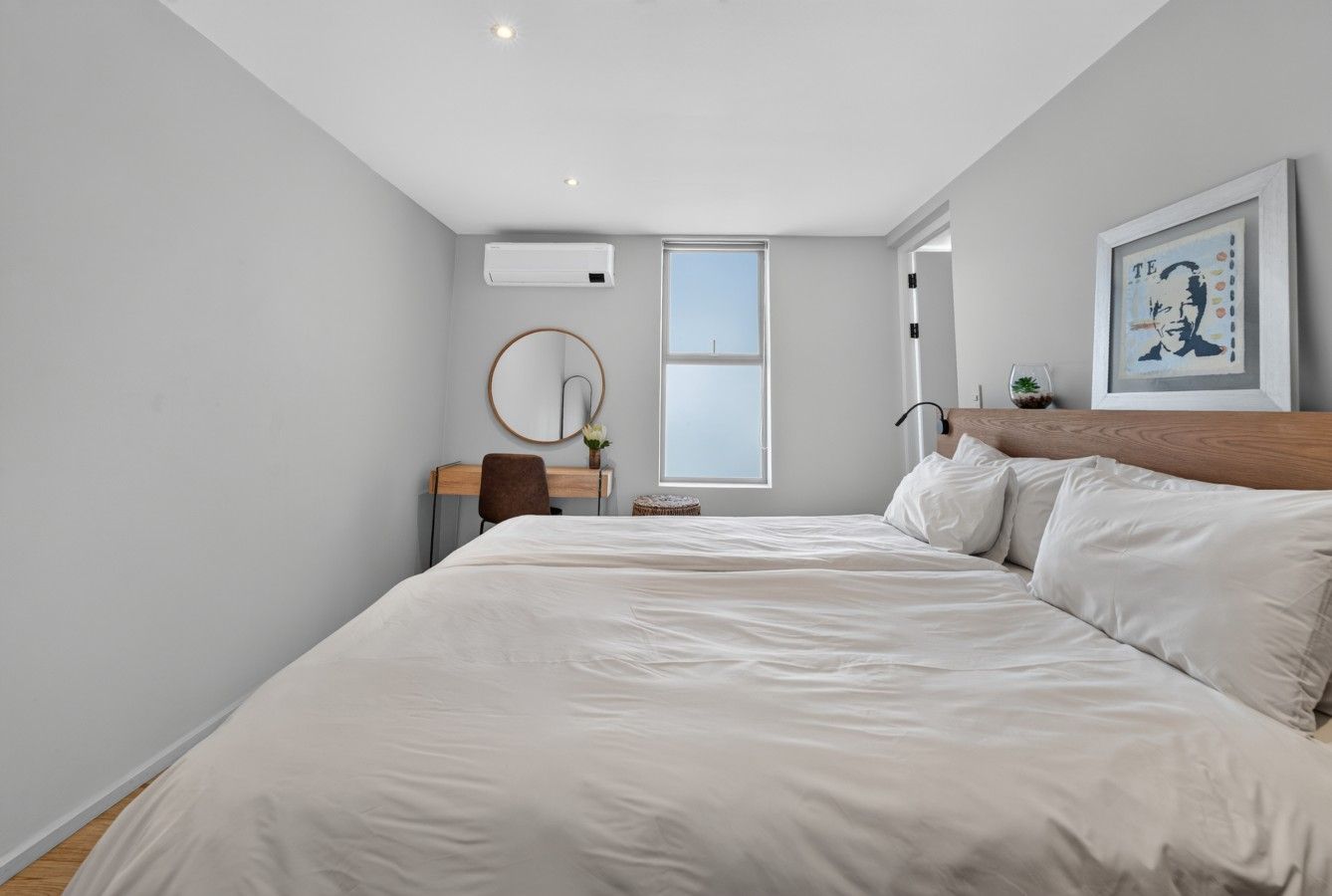 Un dormitorio con una cama grande, un escritorio, una silla, un espejo redondo y una ventana.