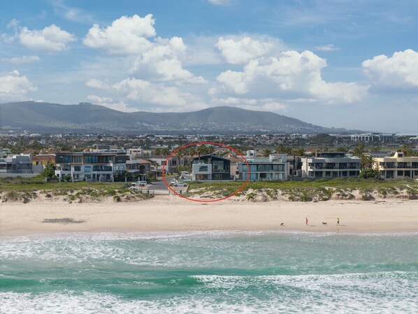 A coastal residential area with modern houses, a beach, and a mountain in the background.
