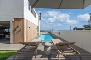 A rooftop pool with wooden deck chairs, a hot tub, and a clear view of the ocean.