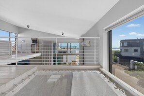 A modern interior with a balcony overlooking a beach, featuring a white color scheme and a view of the sea.