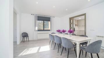 A modern dining area with a white table, grey chairs, and a window with natural light.