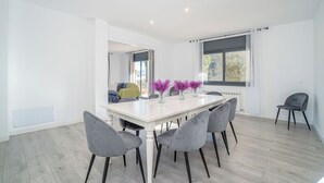 A modern dining area with a white table, grey chairs, and purple flowers. - Jouvacations Villa Rodil (Figueres)