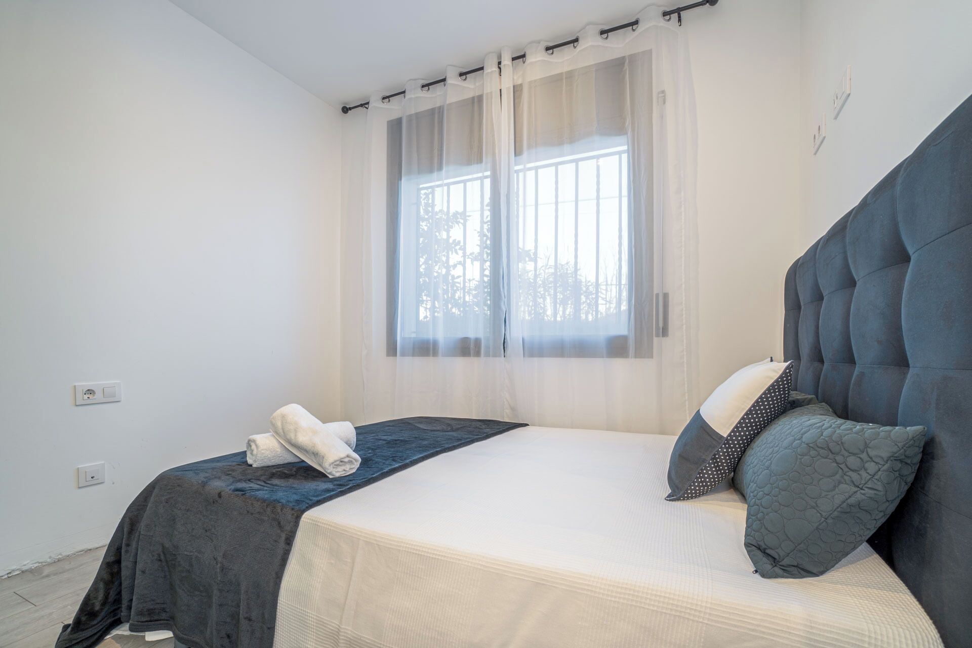 Un dormitorio con cama, ventana con cortinas translúcidas y una toalla sobre la cama.