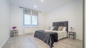 A modern bedroom with a large bed, two bedside tables, a radiator, and sheer curtains. - Jouvacations Villa Rodil (Figueres)