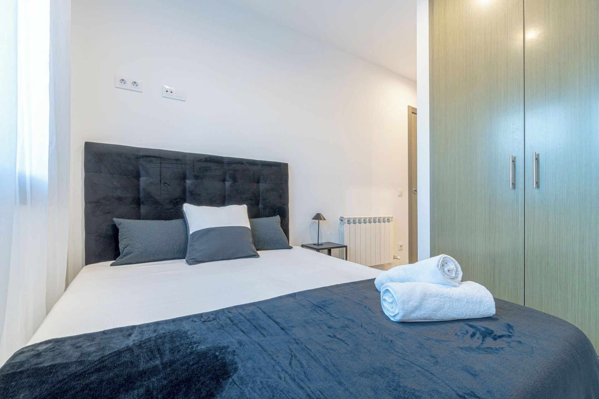 A bedroom with a bed, a nightstand, a radiator, and a wardrobe.