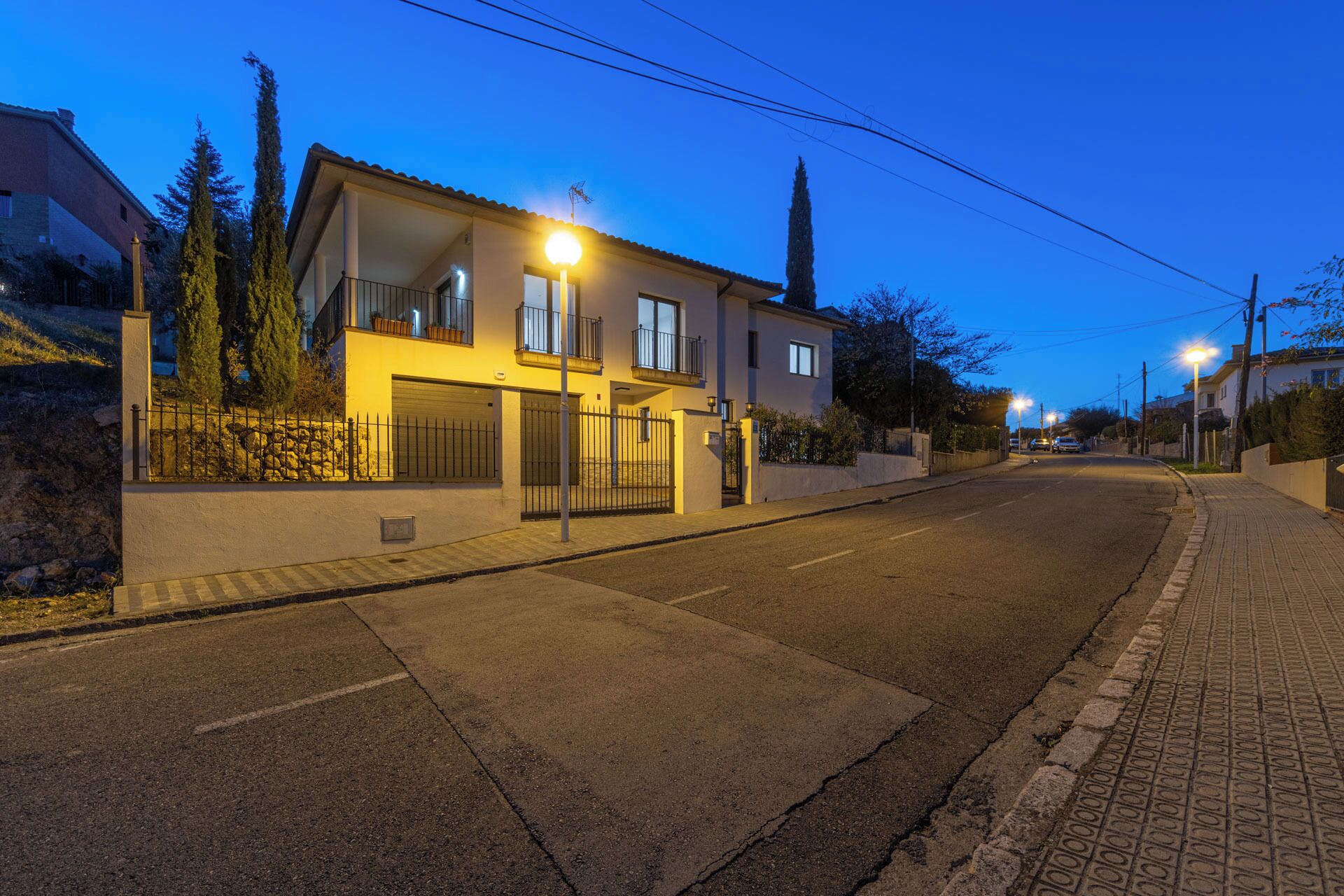 Un immeuble résidentiel à deux étages, doté d’un garage, d’un balcon et situé dans une rue bien éclairée au crépuscule.
