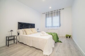 A bedroom with a bed, a nightstand, a lamp, a window with curtains, and a radiator. - Jouvacations Villa Rodil (Figueres)