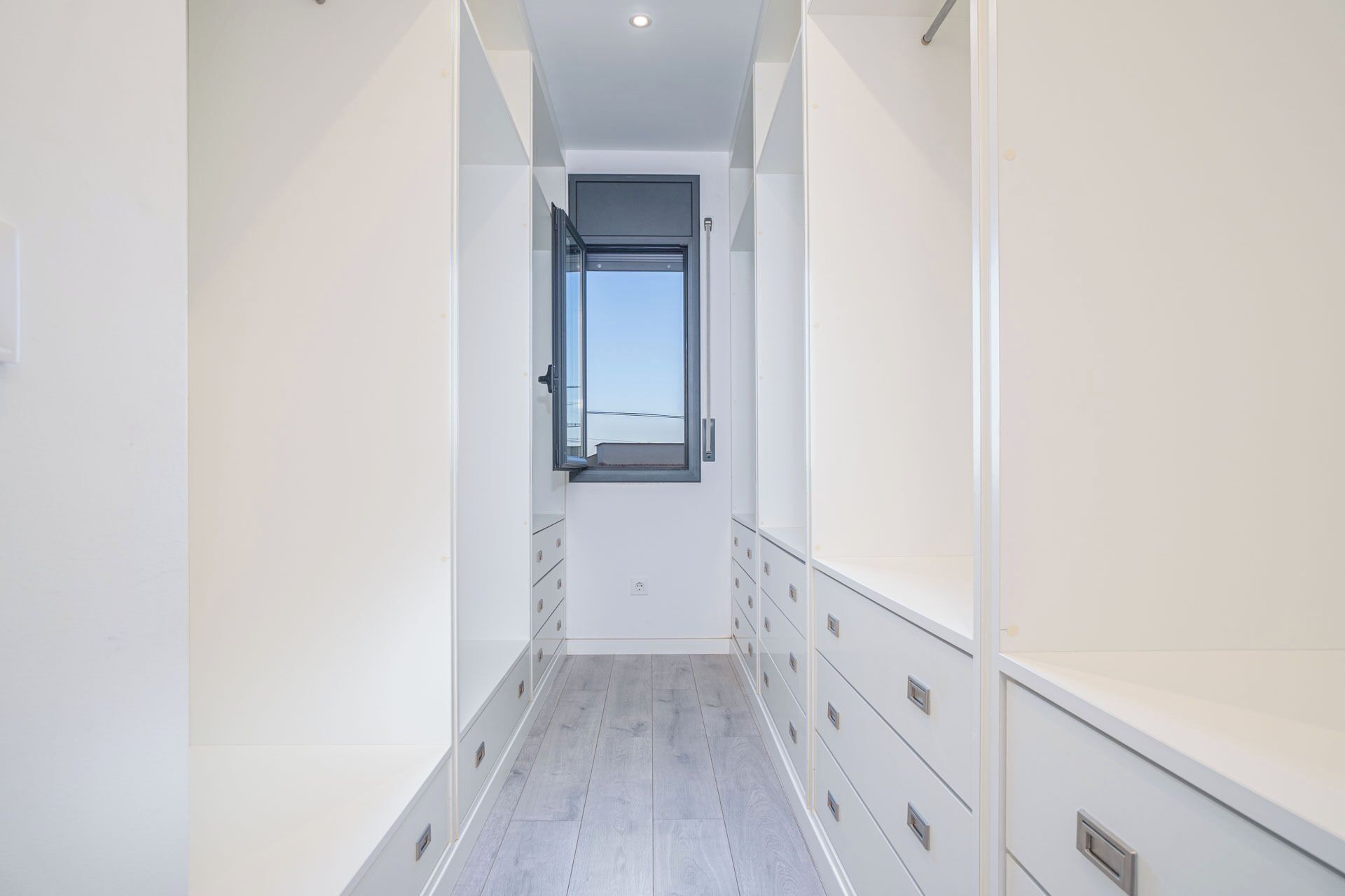 A narrow hallway with a window at the end, leading to a door.