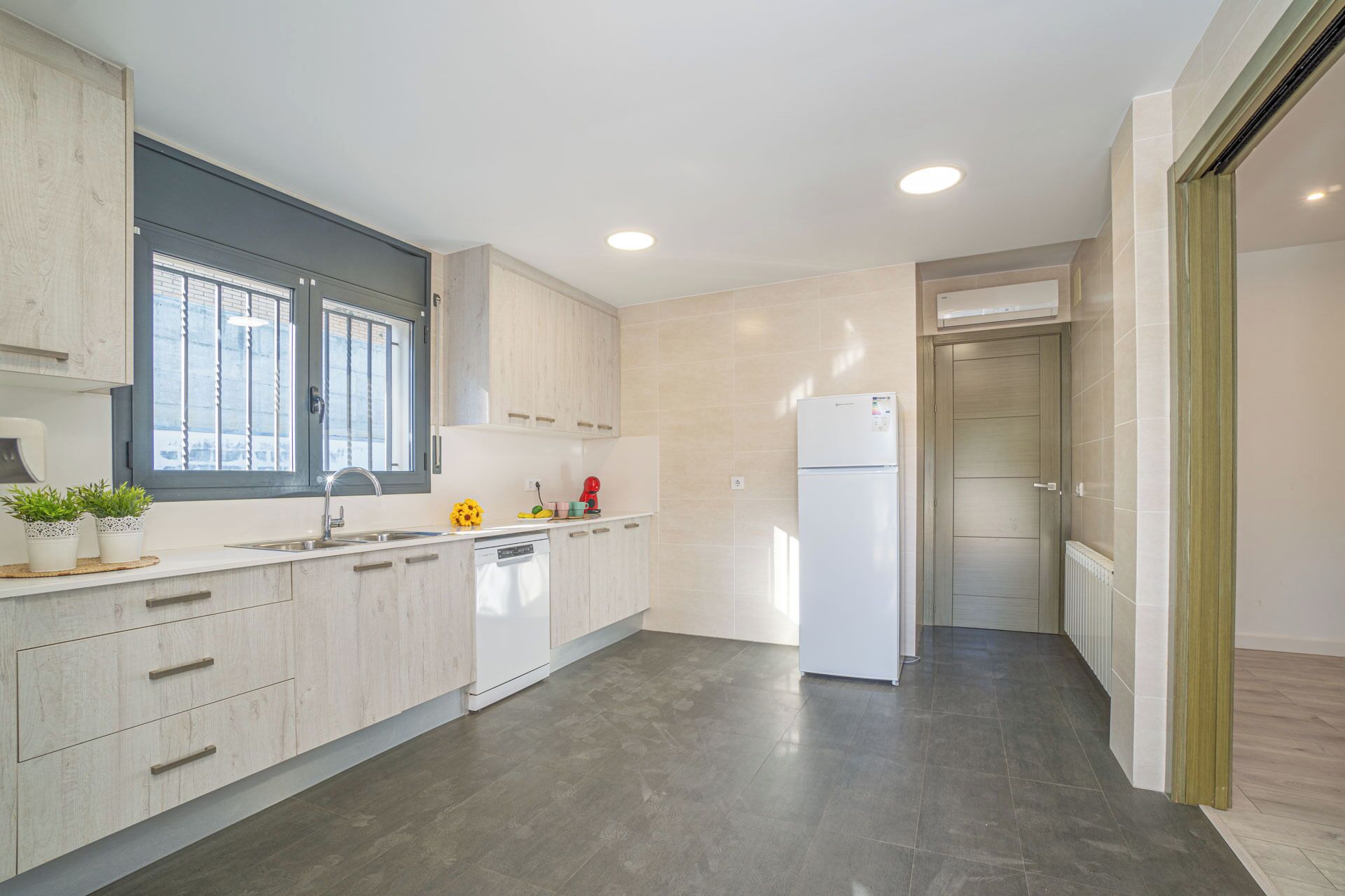 A modern kitchen with light wood cabinets, a white dishwasher, and a built-in refrigerator.