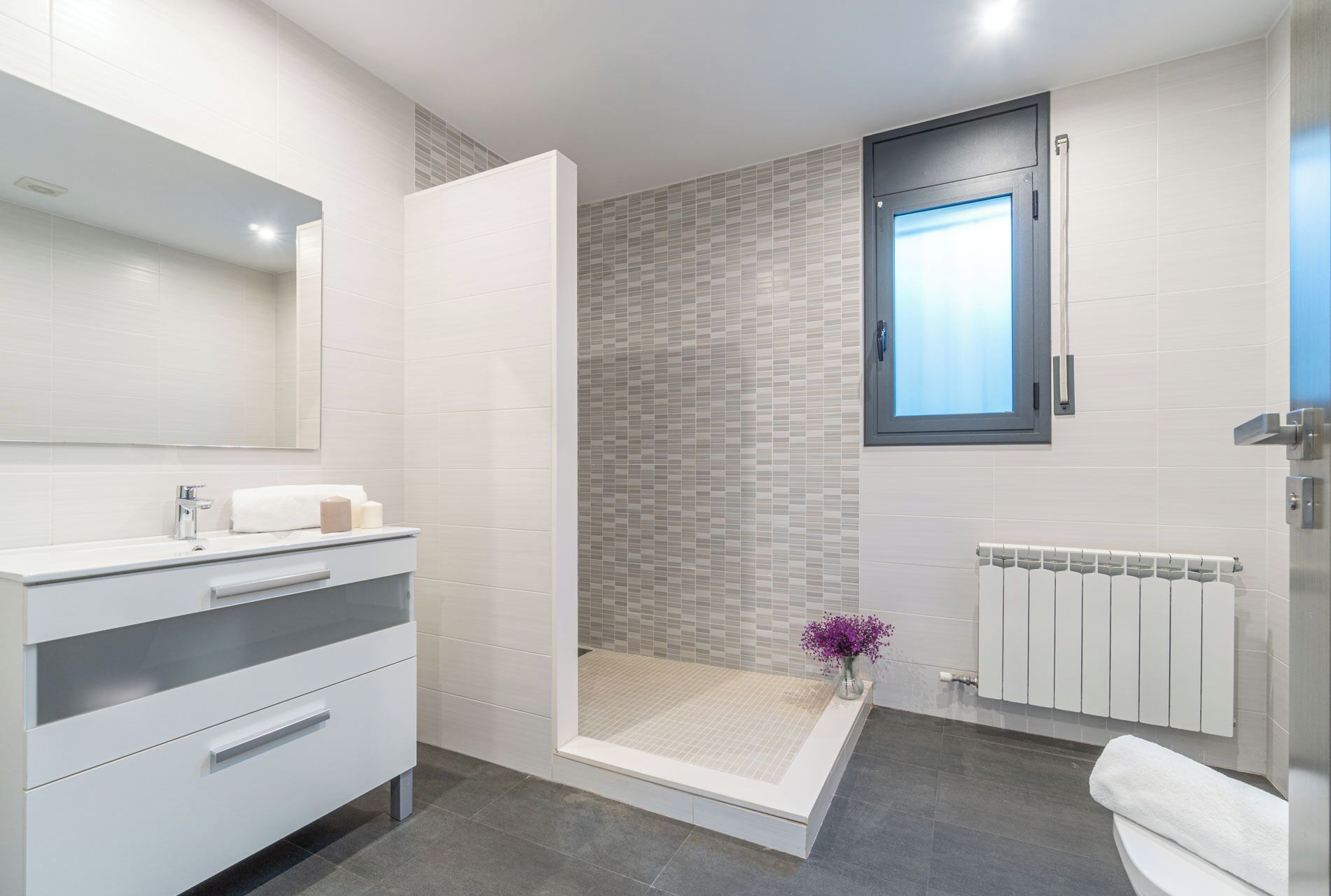 Un baño moderno con ducha a ras de suelo, un espejo grande, un inodoro y un radiador.