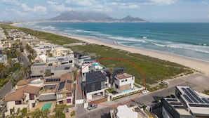 A coastal residential area with modern houses, a beach, and a mountain in the background. - Ocean 9 - Pool-Suite (Cape Town)