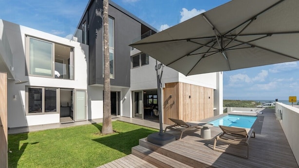 A modern house with a swimming pool, outdoor furniture, and a large umbrella. - Ocean 9 - Pool-Suite (Cape Town)