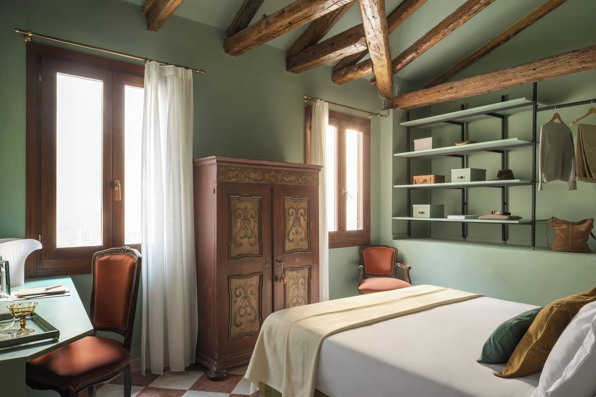 A room with a bed, a desk, a chair, a wardrobe, and shelves with items.