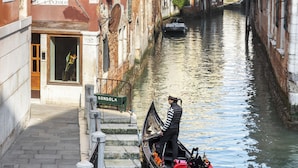 Un canal étroit où sont amarrées des gondoles, des bâtiments dotés de balcons et un panneau indiquant « GONDOLA », signalant un service de transport fluvial.