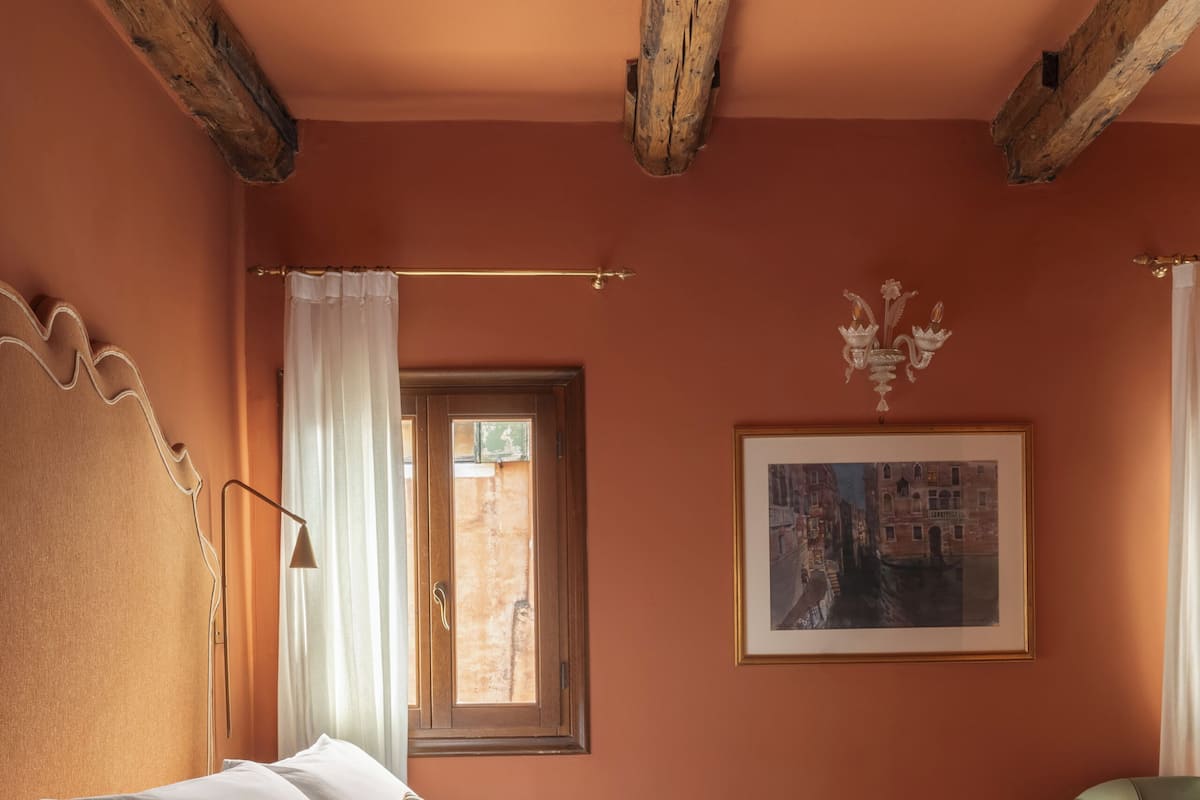 A bedroom with a bed, a window with curtains, a framed picture on the wall, and a green chair.