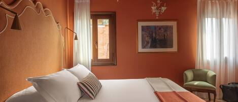 A hotel room with a large bed, a chair, a window with curtains, and a painting on the wall.