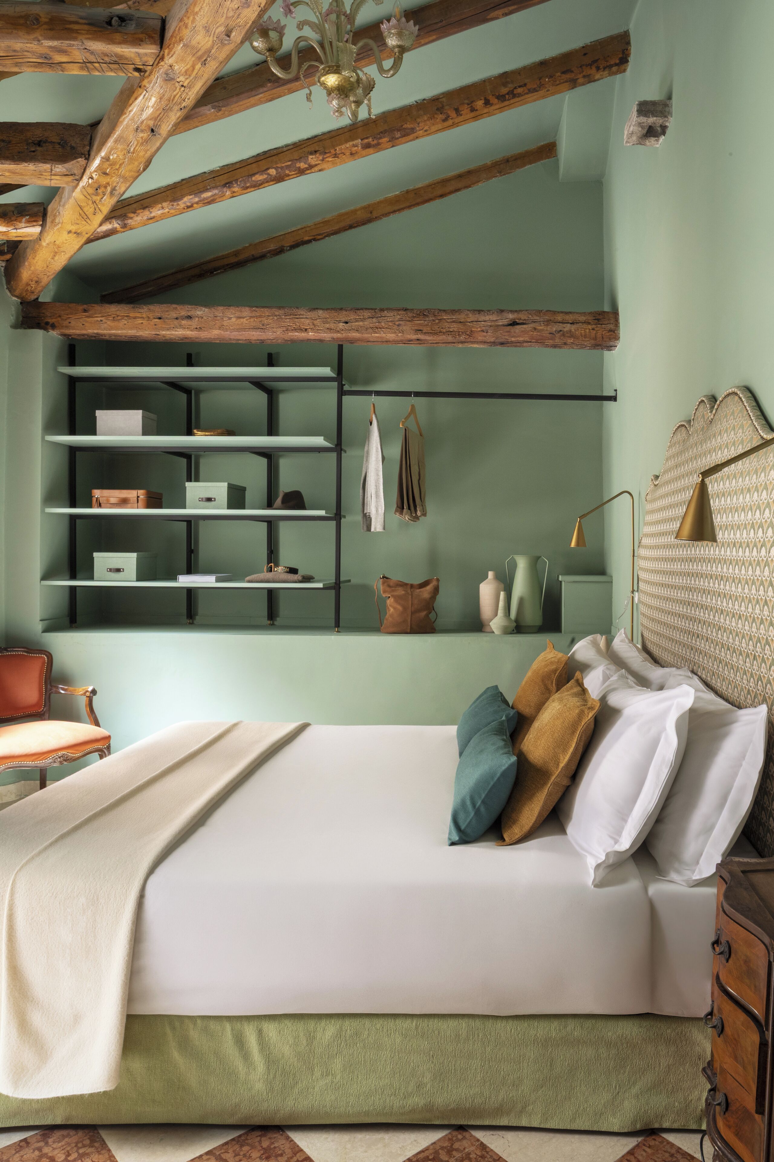 A bedroom with a bed, a dresser, a shelf unit, and a chandelier.