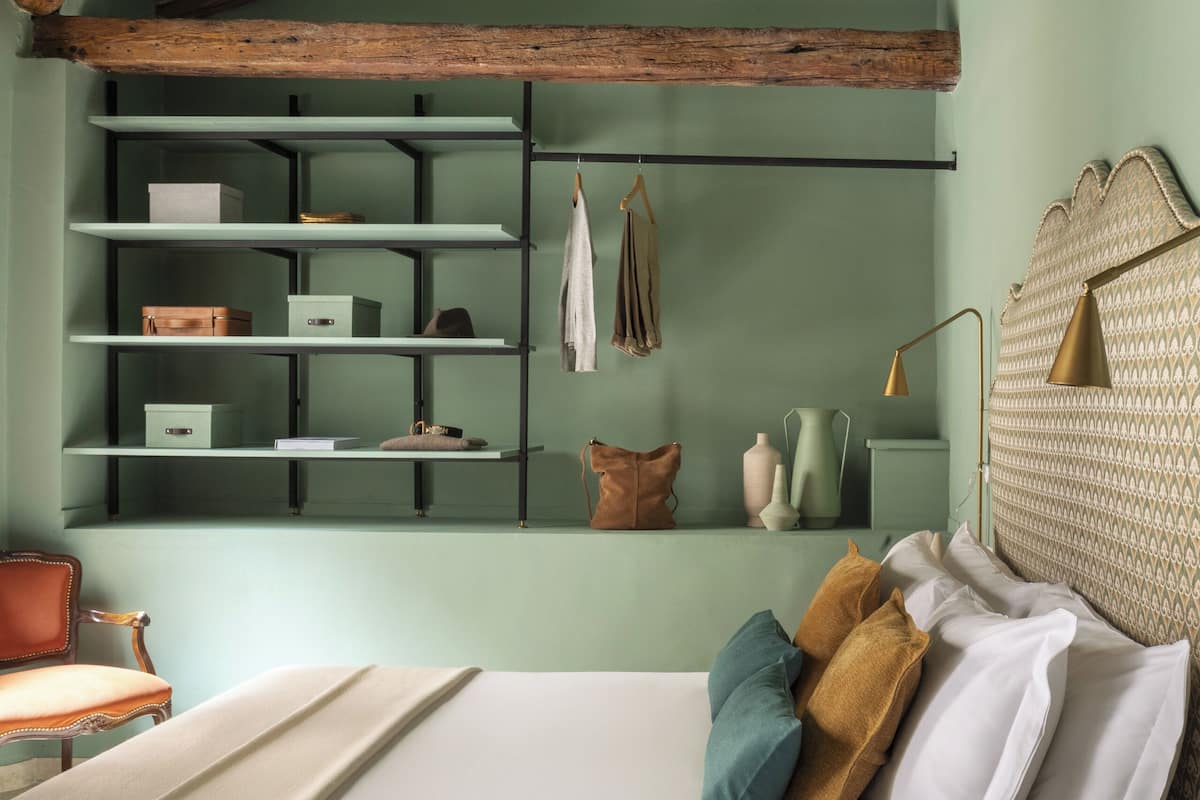 A bedroom with a bed, a dresser, a shelf unit, and a chandelier.