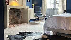 A bedroom with a stone fireplace, a bed, a blue chair, and a cowhide rug. - Guest Room Bleue - Auberge Radieuse (Azay-le-Rideau)
