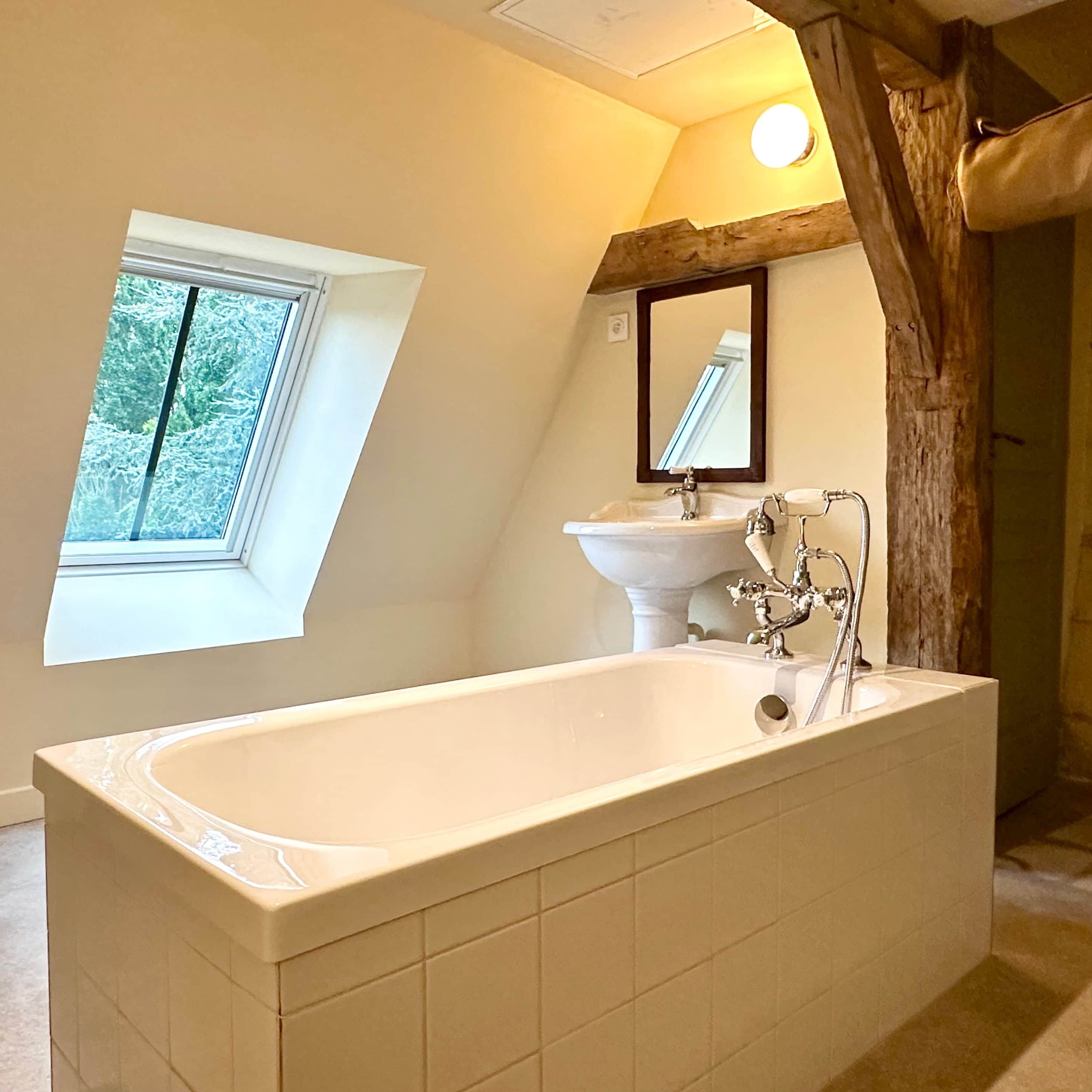 A bathroom with a freestanding bathtub, a window, and a sink with a mirror above it.