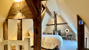 A cozy attic bedroom with exposed wooden beams, a bed, a small table, and a wall-mounted light fixture. - Guest Room Pietro - Auberge Radieuse (Azay-le-Rideau)