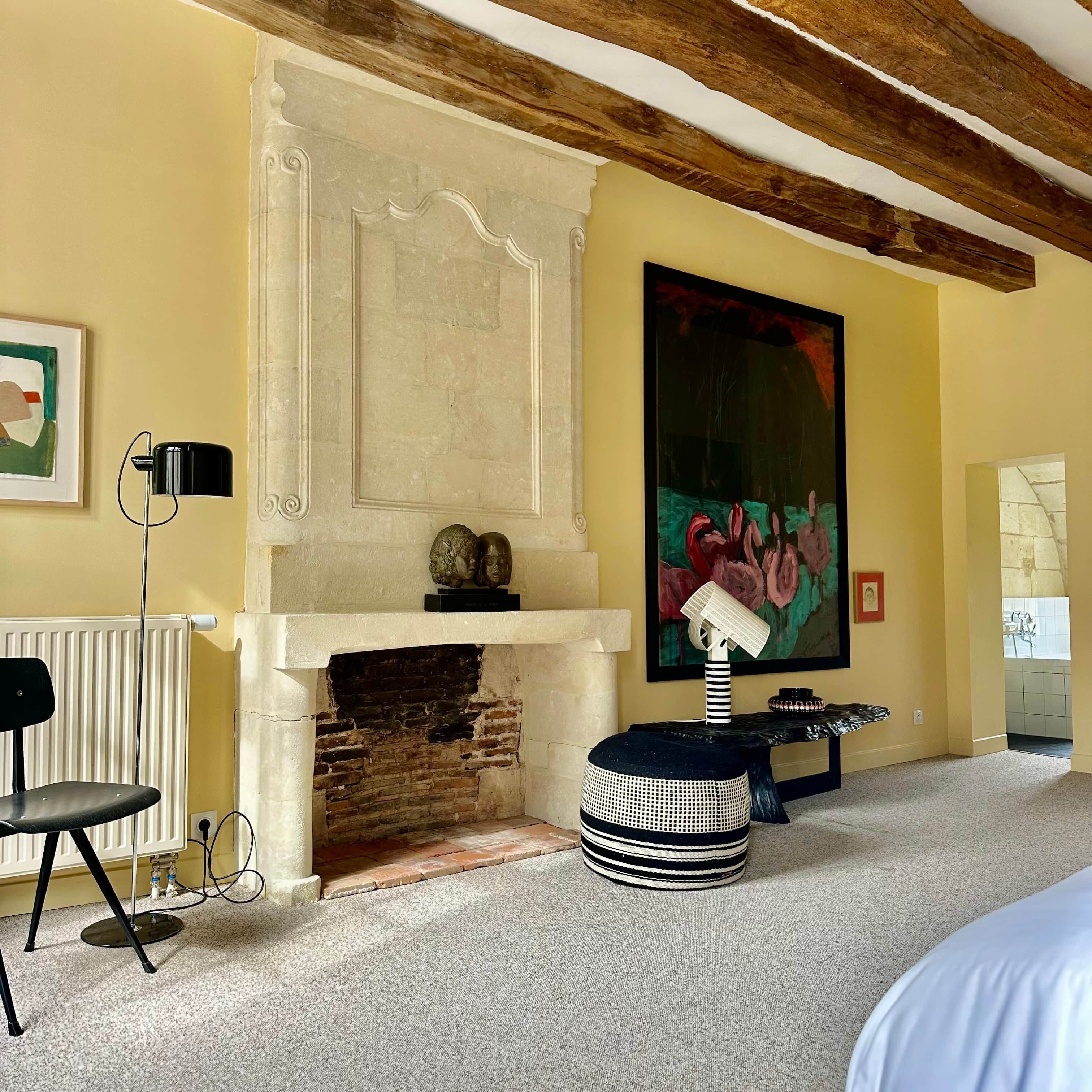 A room with a fireplace, a large abstract painting, a black chair, and a round ottoman.