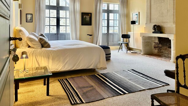 A bedroom with a bed, a chair, a fireplace, and a large window. - Guest room Jaune - Auberge Radieuse (Azay-le-Rideau)