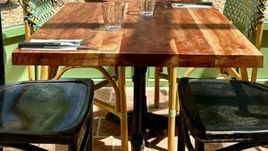 Un espace de restauration en plein air avec une table et des chaises en bois, entouré de verdure et d’un mur en pierre.